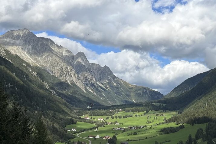 Berglandschaft mit grünen Wiesen und Wolken am Himmel.